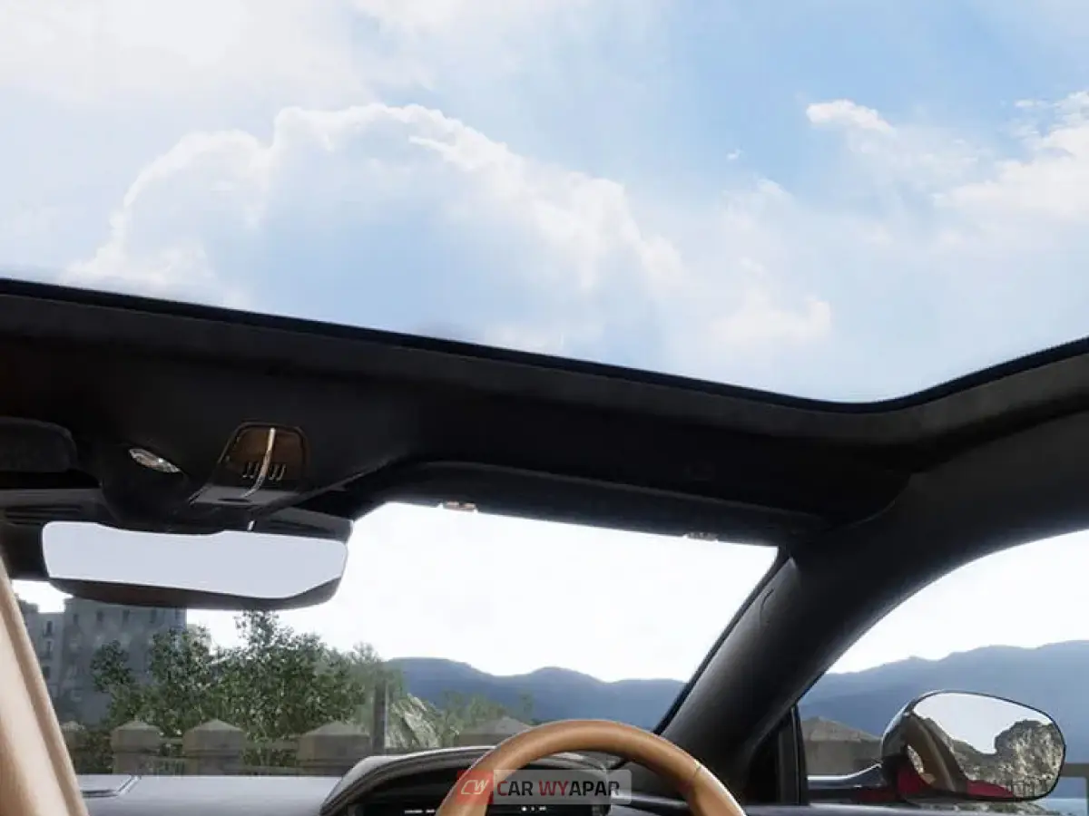 An interior view looking up through the DB12's expansive panoramic glass roof, revealing a bright blue sky with soft white clouds, emphasizing the cabin's airy and open feel.
